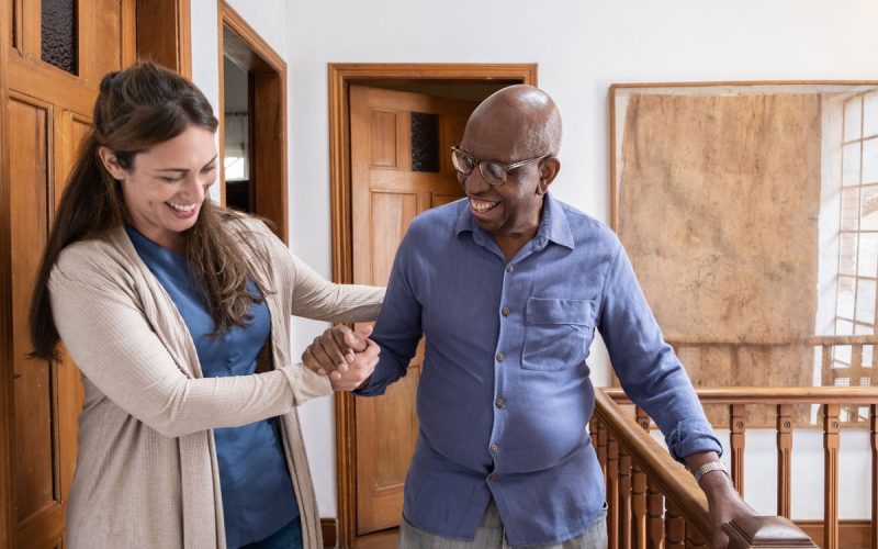 Home caregiver helping senior man walking at home